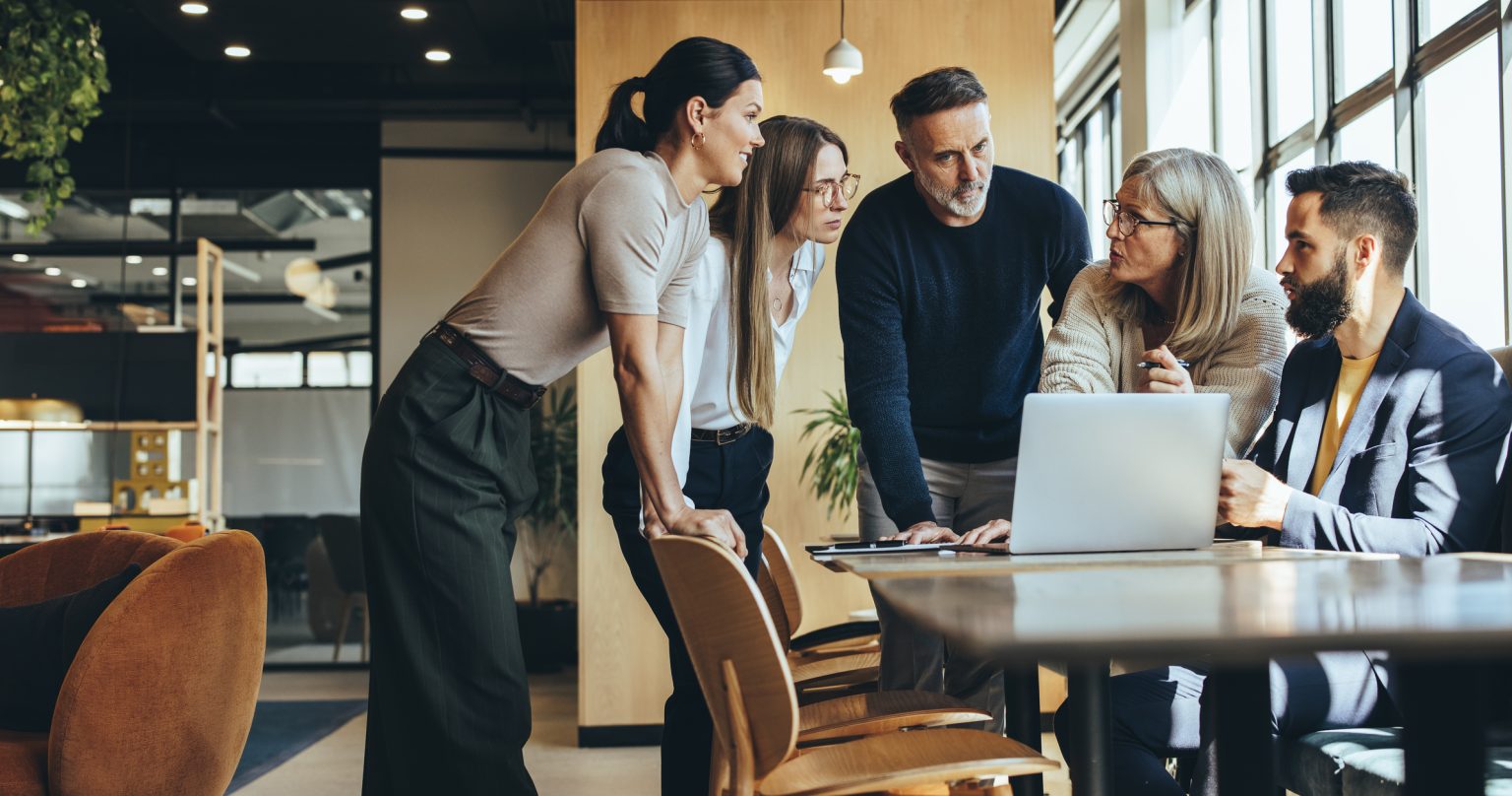 a group of people inspecting something on a laptop in an office