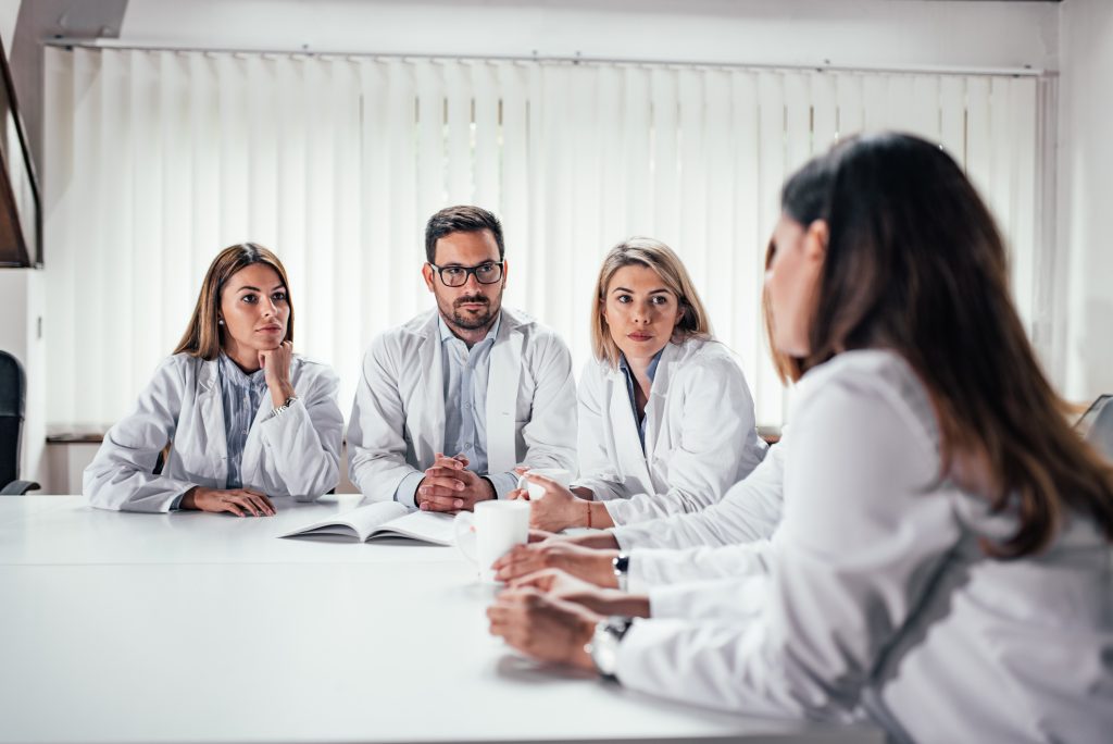 photograph of people in lab coats around a conference table having a discussion
